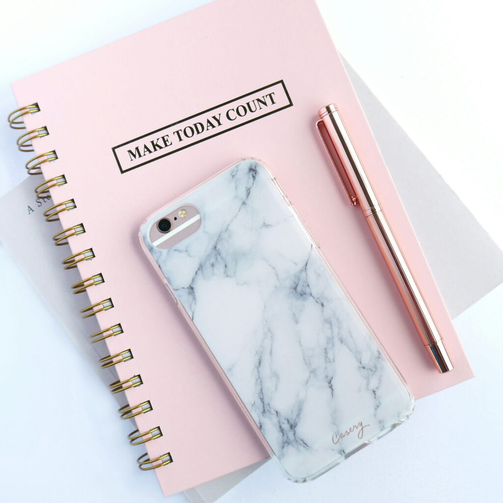 A pink notebook is shown with a phone laying downward on top of it to denote a workbook for ADA Title II needs guide