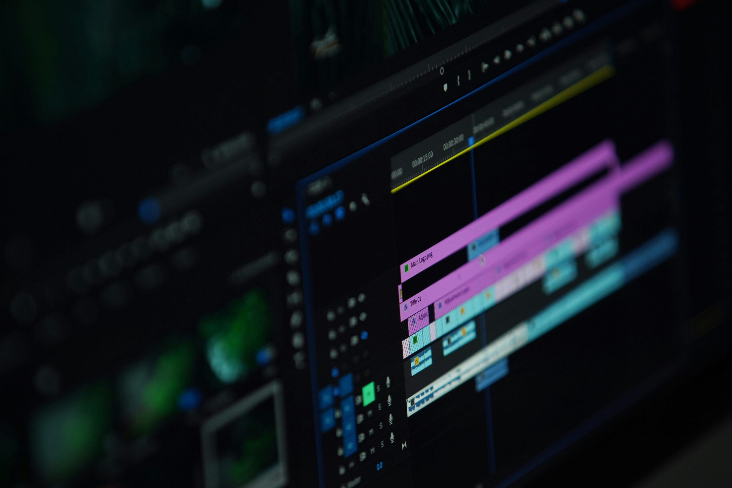 A close-up, angled shot of a computer monitor displaying a professional video editing software timeline. Colorful, horizontal video and audio tracks in shades of purple and blue are visible, with the focus softly blurring toward the background.