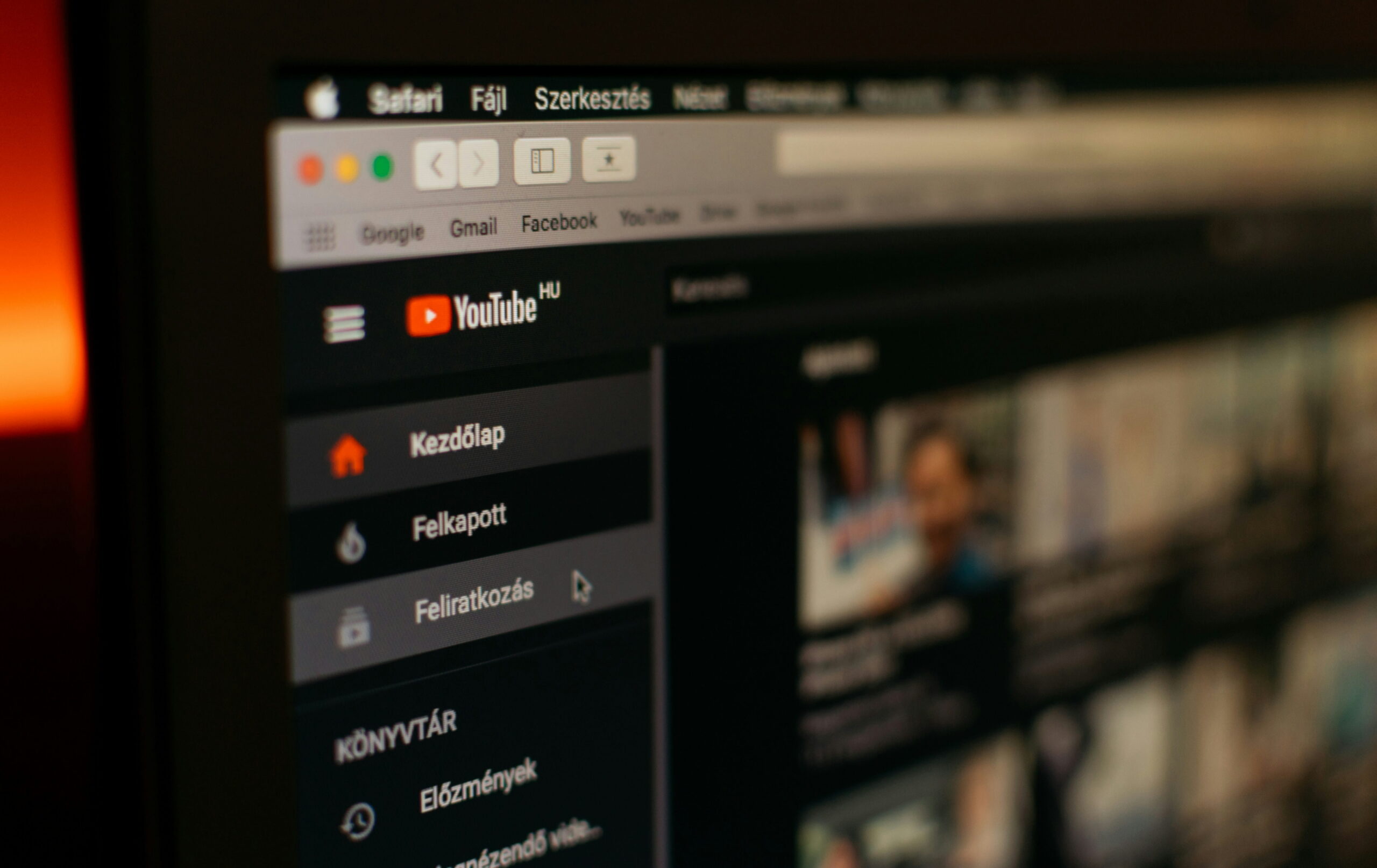 A close-up, shallow-depth-of-field shot of a laptop screen displaying the YouTube homepage in Hungarian. The sidebar navigation shows terms like "Kezdőlap" (Home) and "Felkapott" (Trending) next to the YouTube logo, with a warm, out-of-focus light glowing in the background.