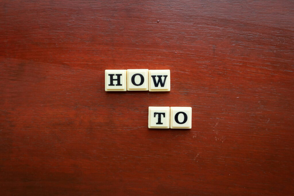 Scrabble-style letter tiles spelling out the words "HOW TO" arranged on a dark wooden surface.