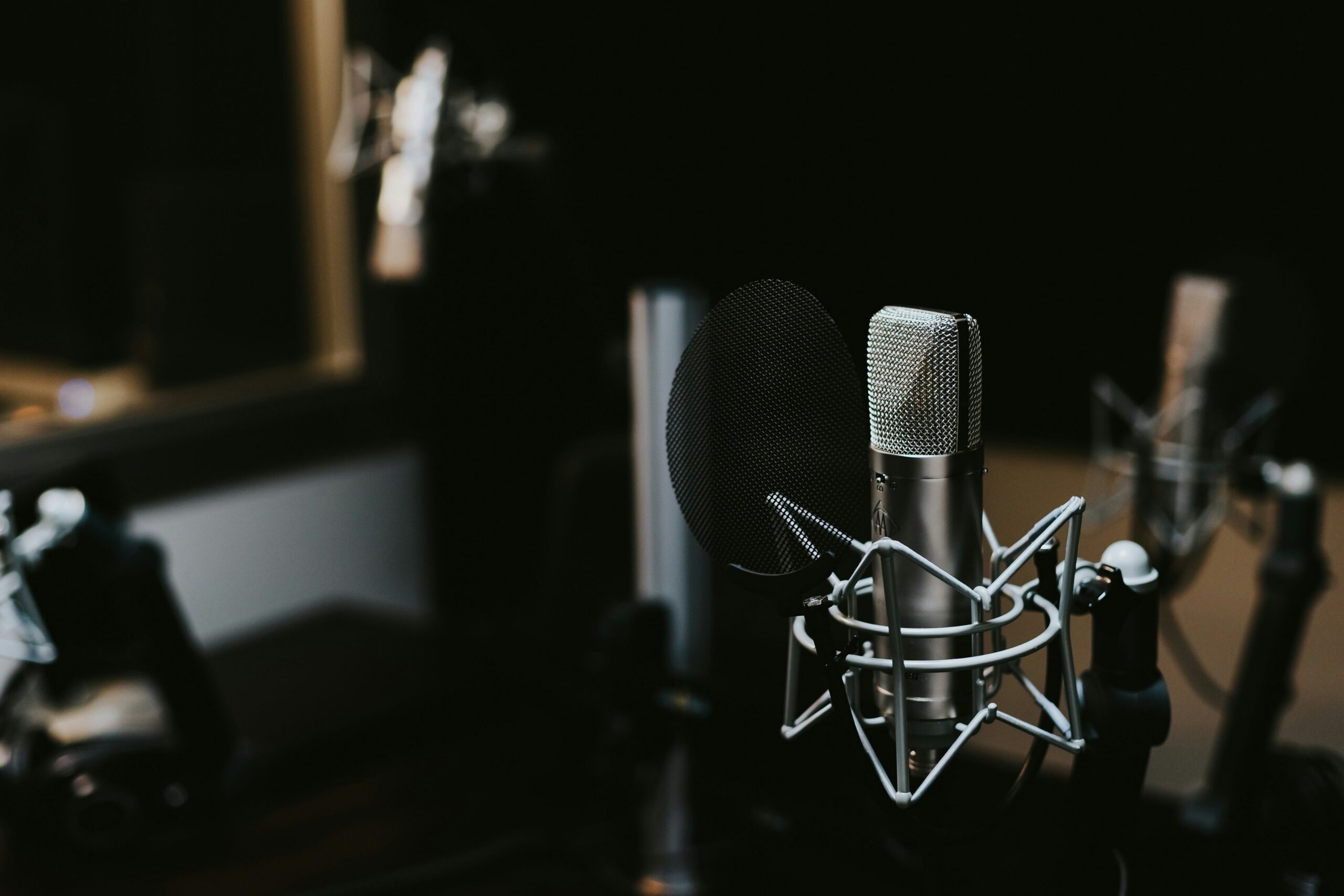 A close-up shot of a professional studio condenser microphone with a pop filter in a dark recording studio.