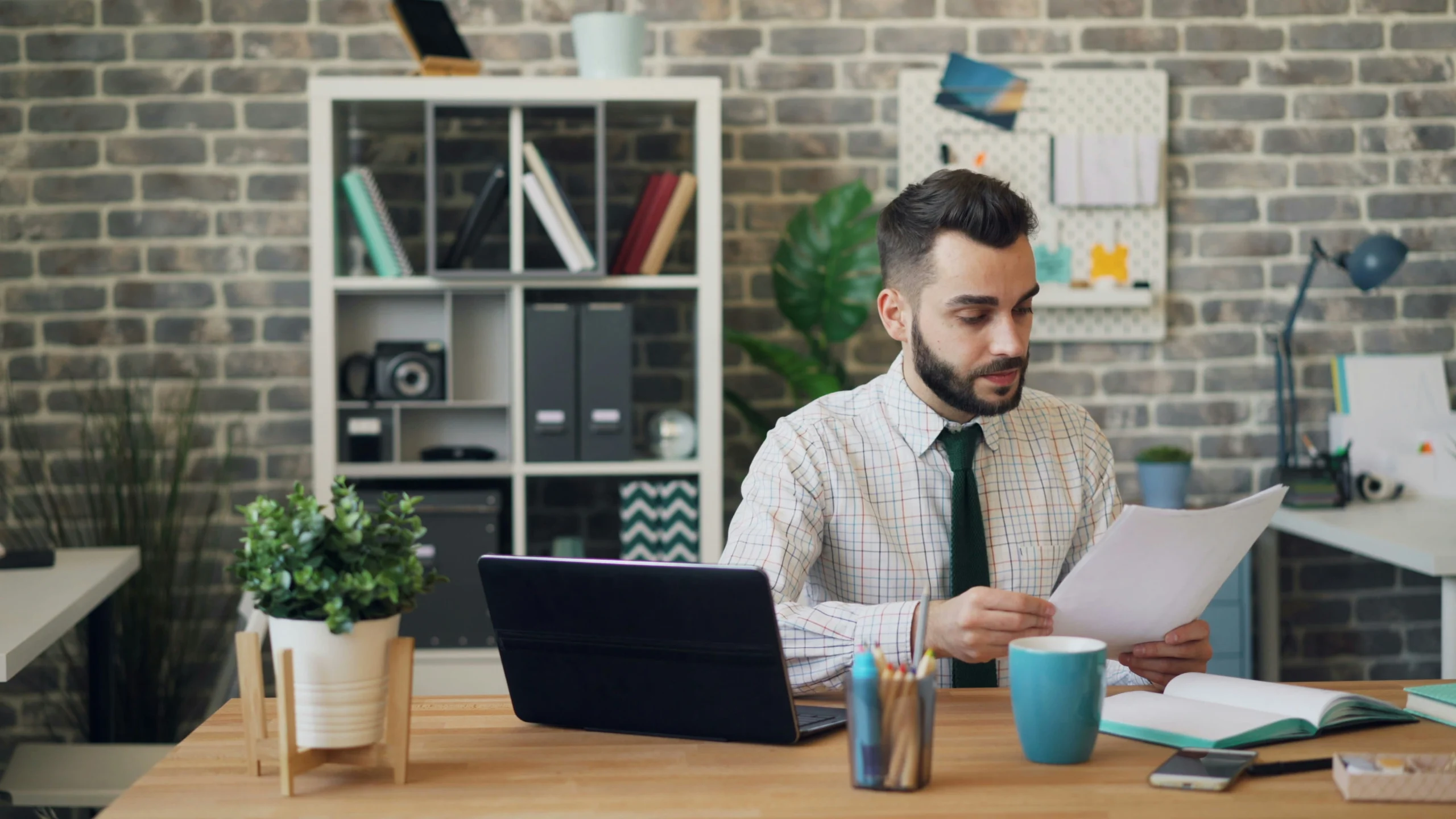 A professional man reviewing printed legal documents at a wooden desk next to a laptop and an organized office bookshelf.