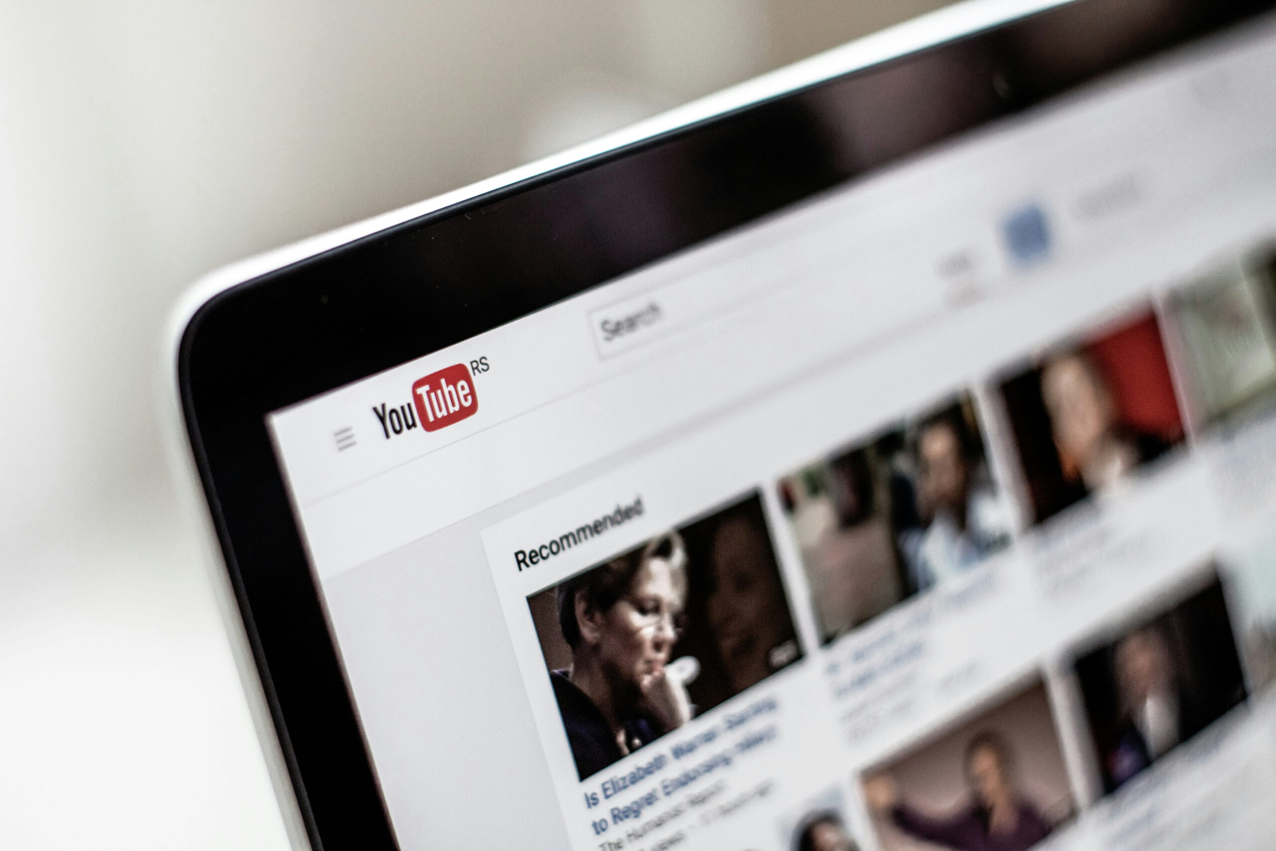 Close-up of a laptop screen showing the YouTube homepage with recommended video thumbnails and the search bar.