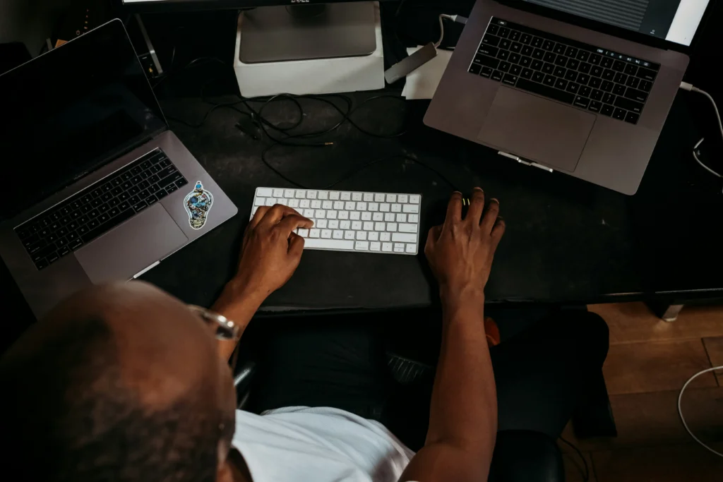 An overhead view of a software engineer working at a dark desk setup featuring multiple laptops, a wireless keyboard, and code on screen.